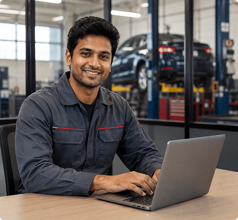 Technician in a blue uniform using a laptop at a desk in an automotive service center