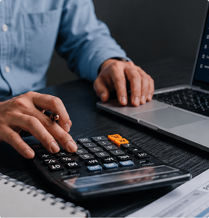 Hands using a calculator and laptop while reviewing a payroll report on a desk