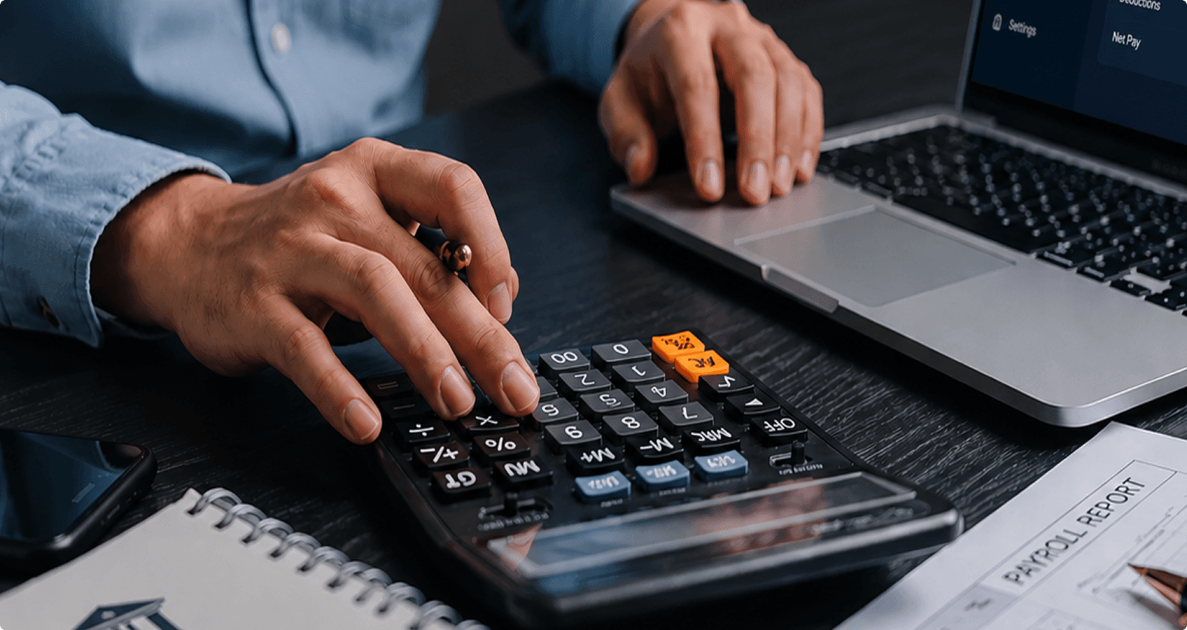 Hands using a calculator and laptop while reviewing a payroll report on a desk