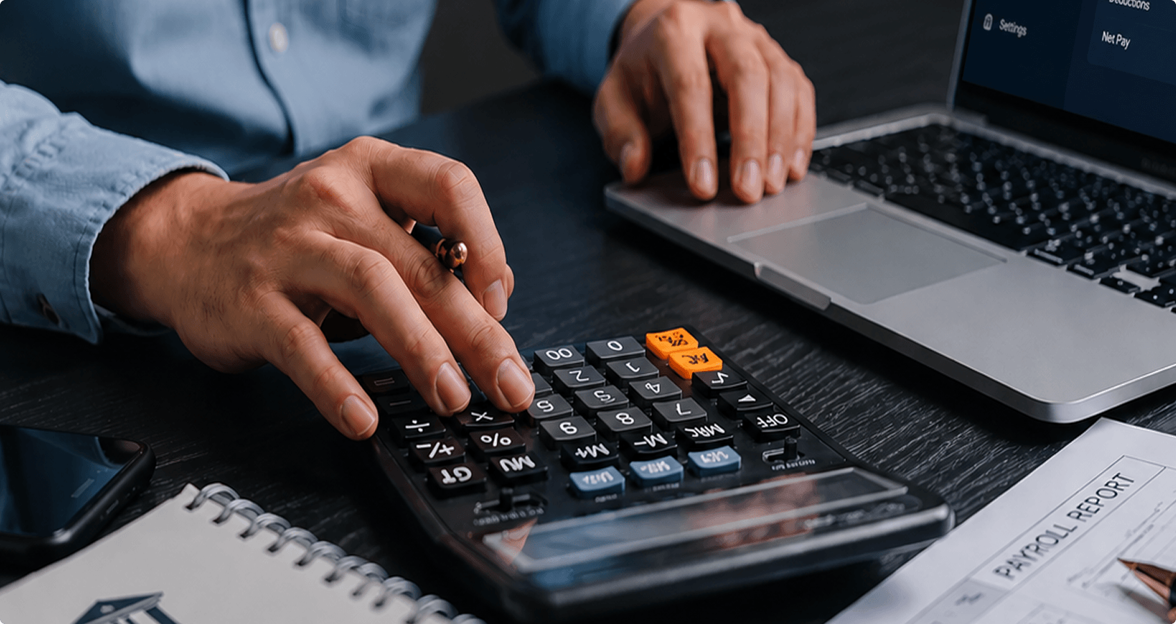 Hands using a calculator and laptop while reviewing a payroll report on a desk