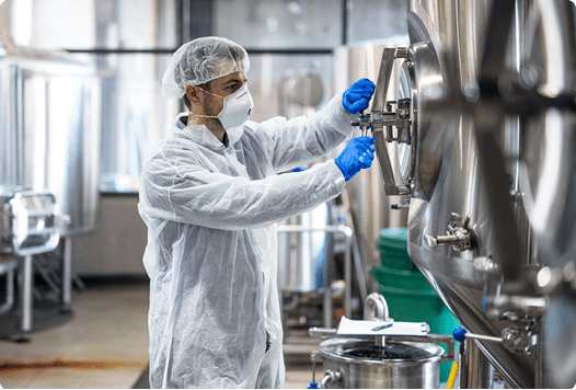 Pharmaceutical plant worker in protective gear operating industrial equipment at a manufacturing facility
