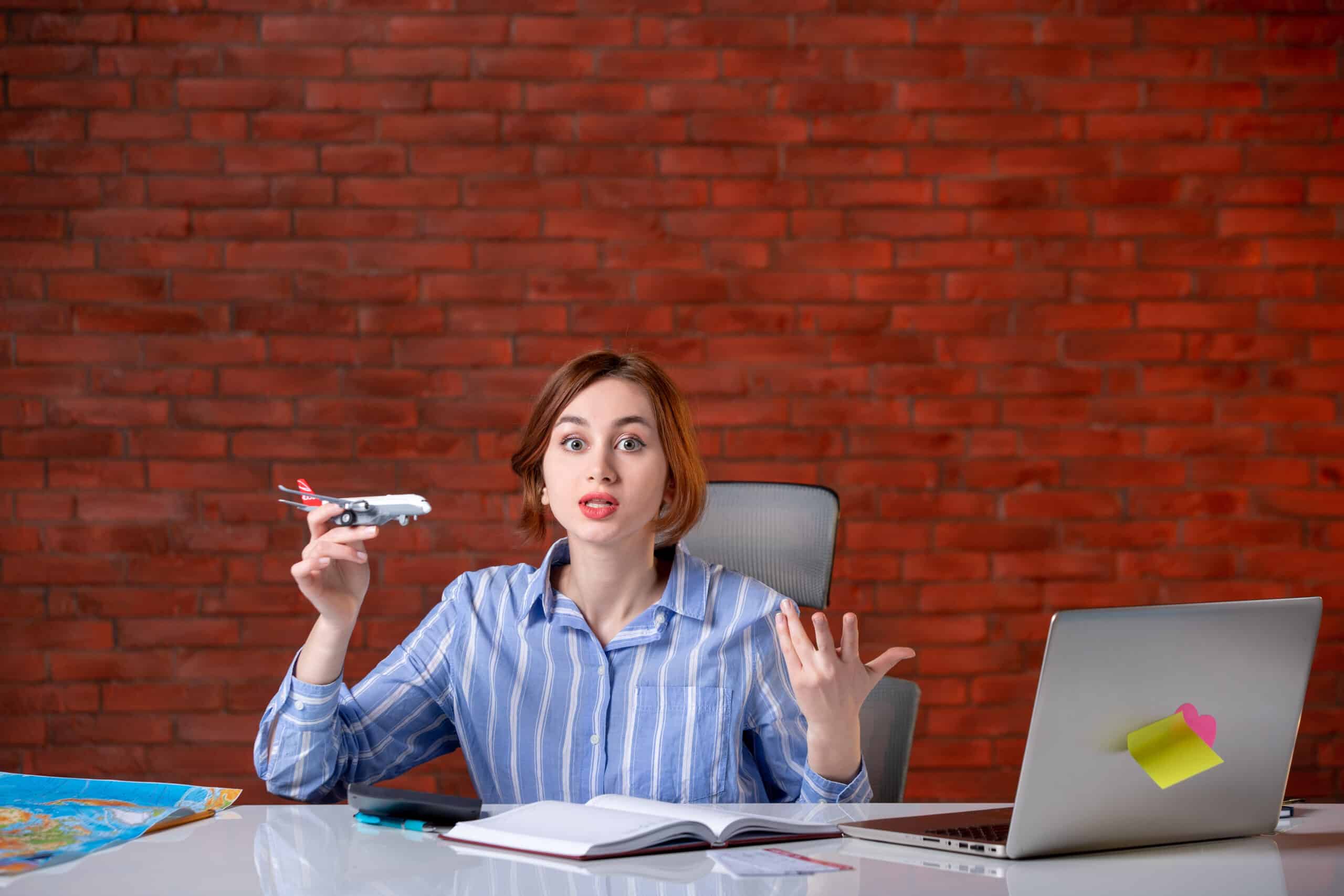 Front view travel agent sitting behind her working place playing with toy plane agency service assistant manager map