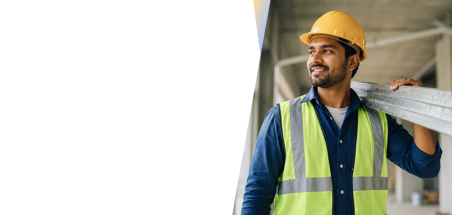 Construction worker in a hard hat and safety vest carrying metal studs at a project site