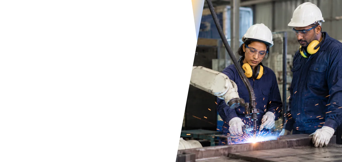 Factory workers in hard hats and safety gear supervising a robotic welding arm with sparks on a manufacturing floor