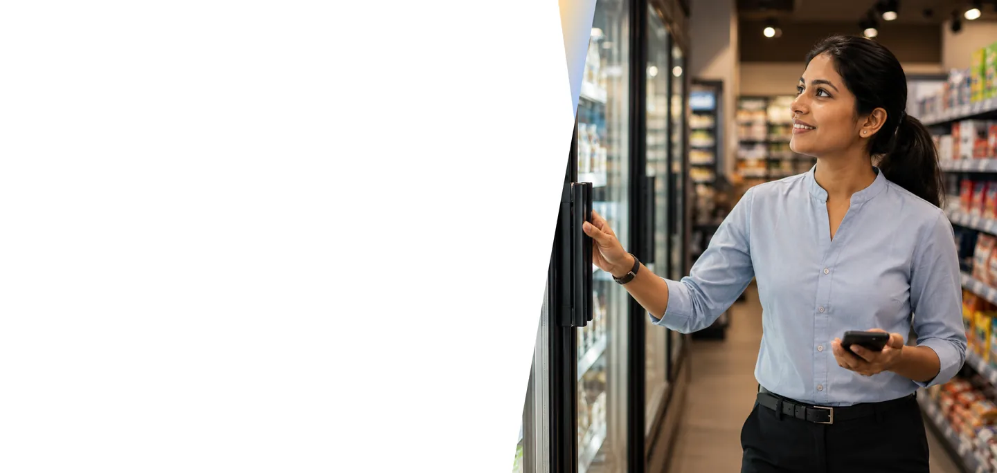Retail store manager holding a smartphone while opening a refrigerated display case in a supermarket