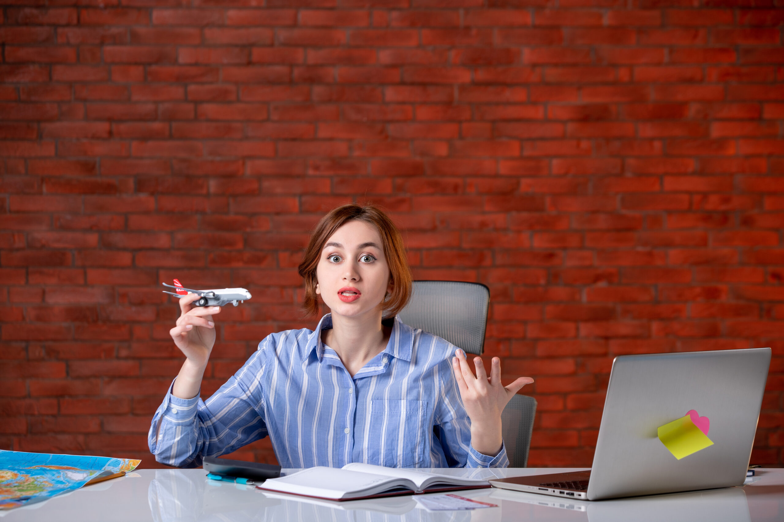 Front view travel agent sitting behind her working place playing with toy plane agency service assistant manager map